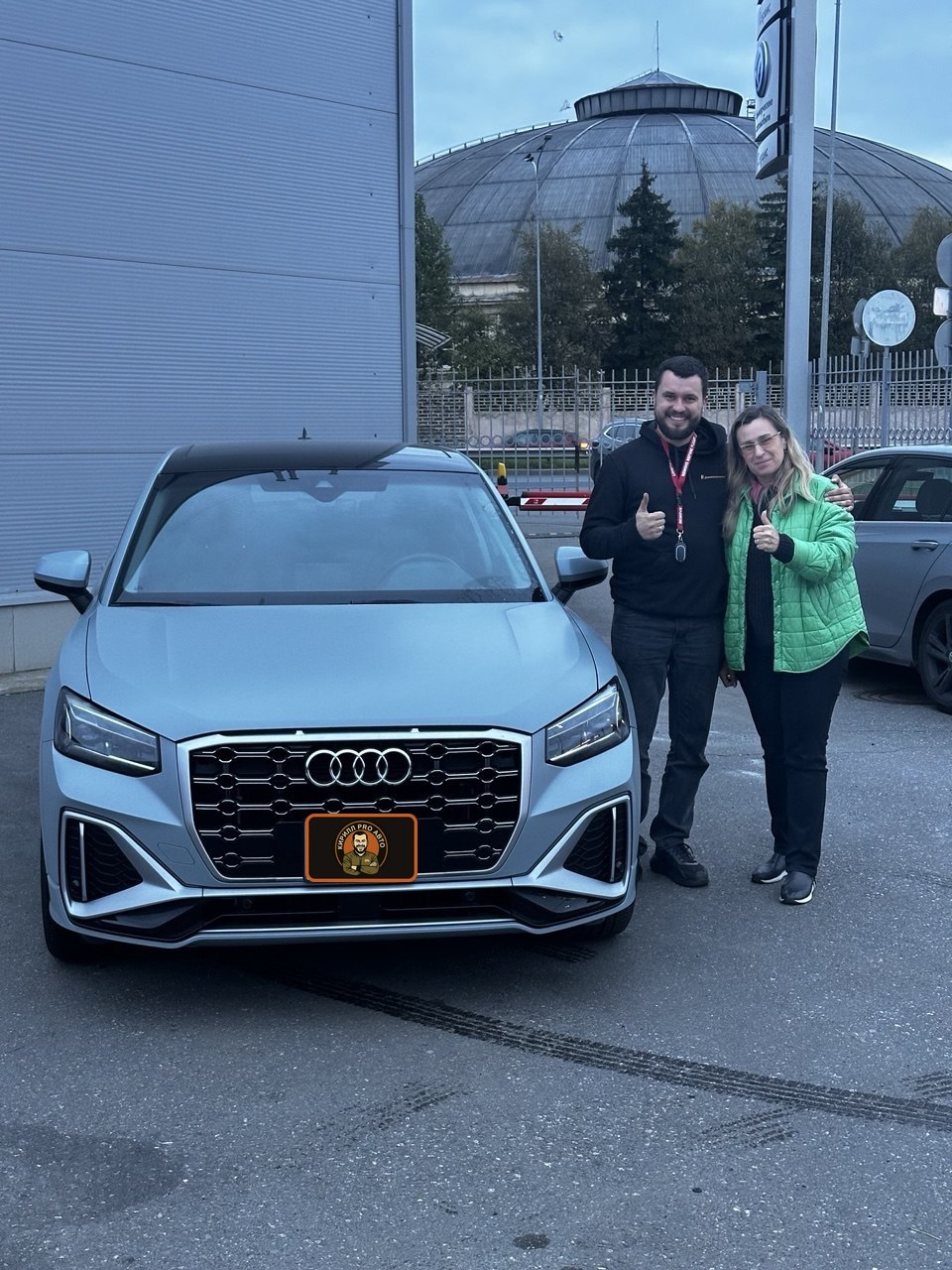Два человека рядом со светлым Audi у здания.